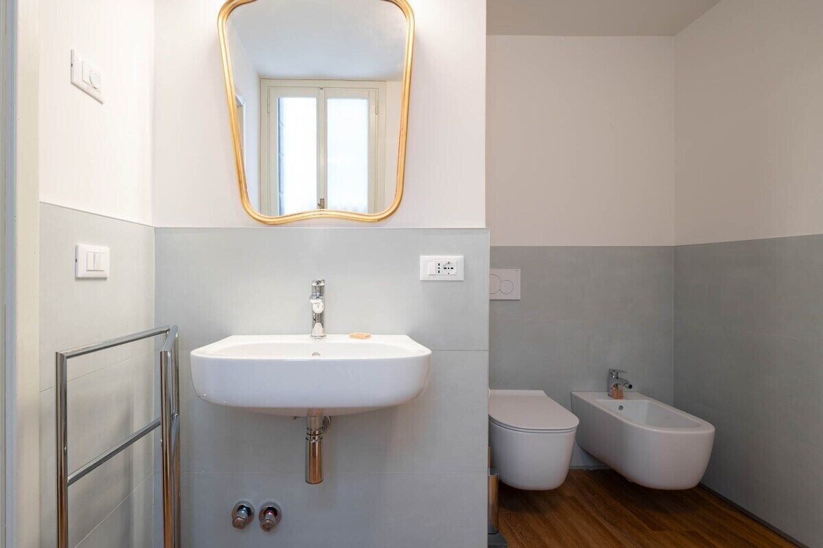 Uma casa de banho moderna com uma pia branca, um espelho com moldura dourada, uma sanita e um bidé.