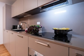 A modern kitchen with a black induction cooktop, a stainless steel range hood, and a single drawer with a handle. - San Beneto (Venezia)
