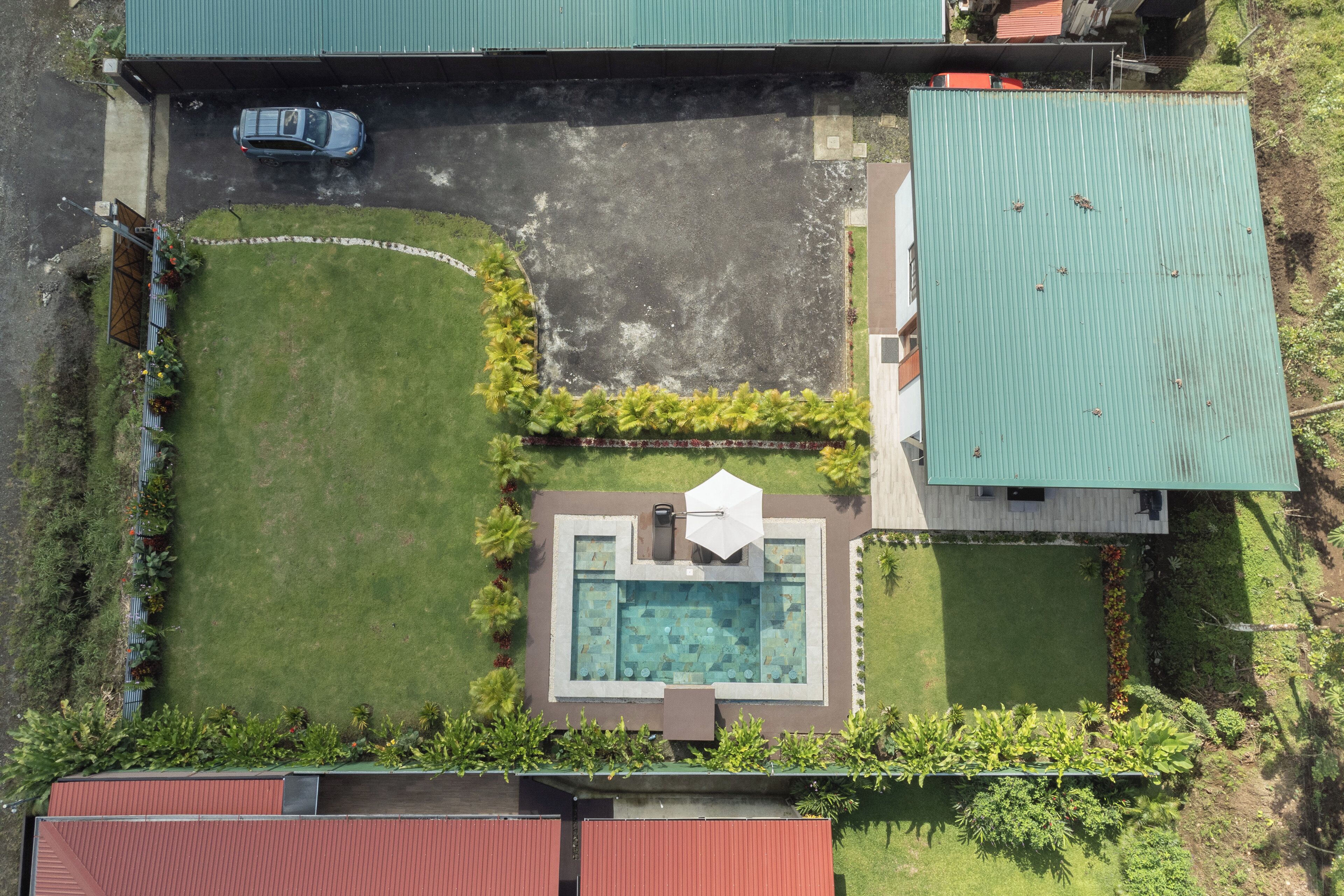 An aerial view of a property with a swimming pool, a covered patio, and a car parked on the street.