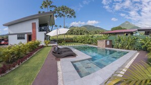 A modern house with a swimming pool, a covered patio, and lush landscaping.