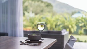 A dining table with a bowl of soup and a glass of water, set against a backdrop of greenery and mountains.