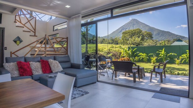 A modern living room with a large sliding glass door leading to an outdoor patio with a view of a mountain.