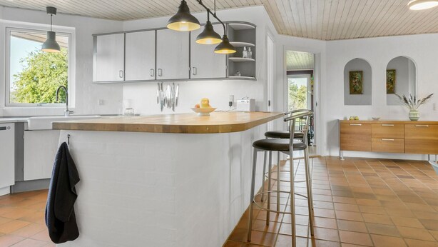 Una cocina moderna con armarios blancos, una isla de madera e iluminación colgante.
