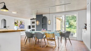 Una cocina moderna con zona de comedor, que cuenta con un amplio ventanal, techo de madera y suelo de baldosas.