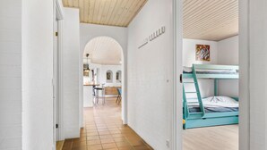 Un pasillo estrecho que da a una habitación con literas, un rincón de cocina y un arco.