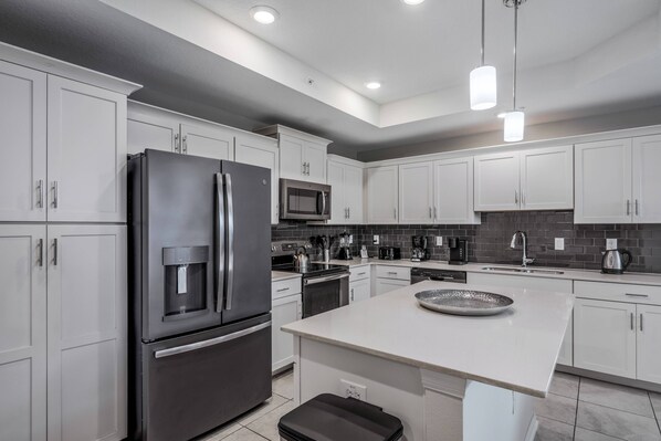 Una cocina moderna con gabinetes blancos, electrodomésticos de acero inoxidable, una isla central e iluminación colgante.