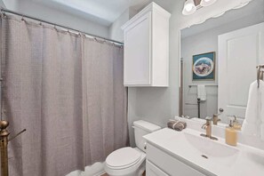 Bathroom features a toilet, sink, and shower curtain, with a framed picture above the mirror.