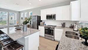 A modern kitchen with white cabinets, stainless steel appliances, and a granite countertop. - Magnolia Haus at Solms Landing (New Braunfels)