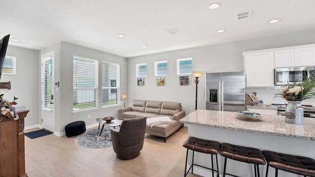 A modern kitchen with a central island, a dining area with bar stools, and a living room with a sofa and a coffee table. - Magnolia Haus at Solms Landing (New Braunfels)