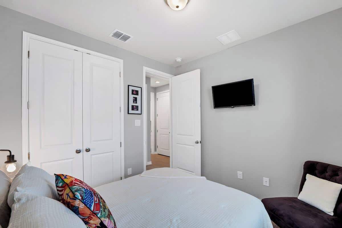 A bedroom with a bed, a TV mounted on the wall, and a door leading to another room.
