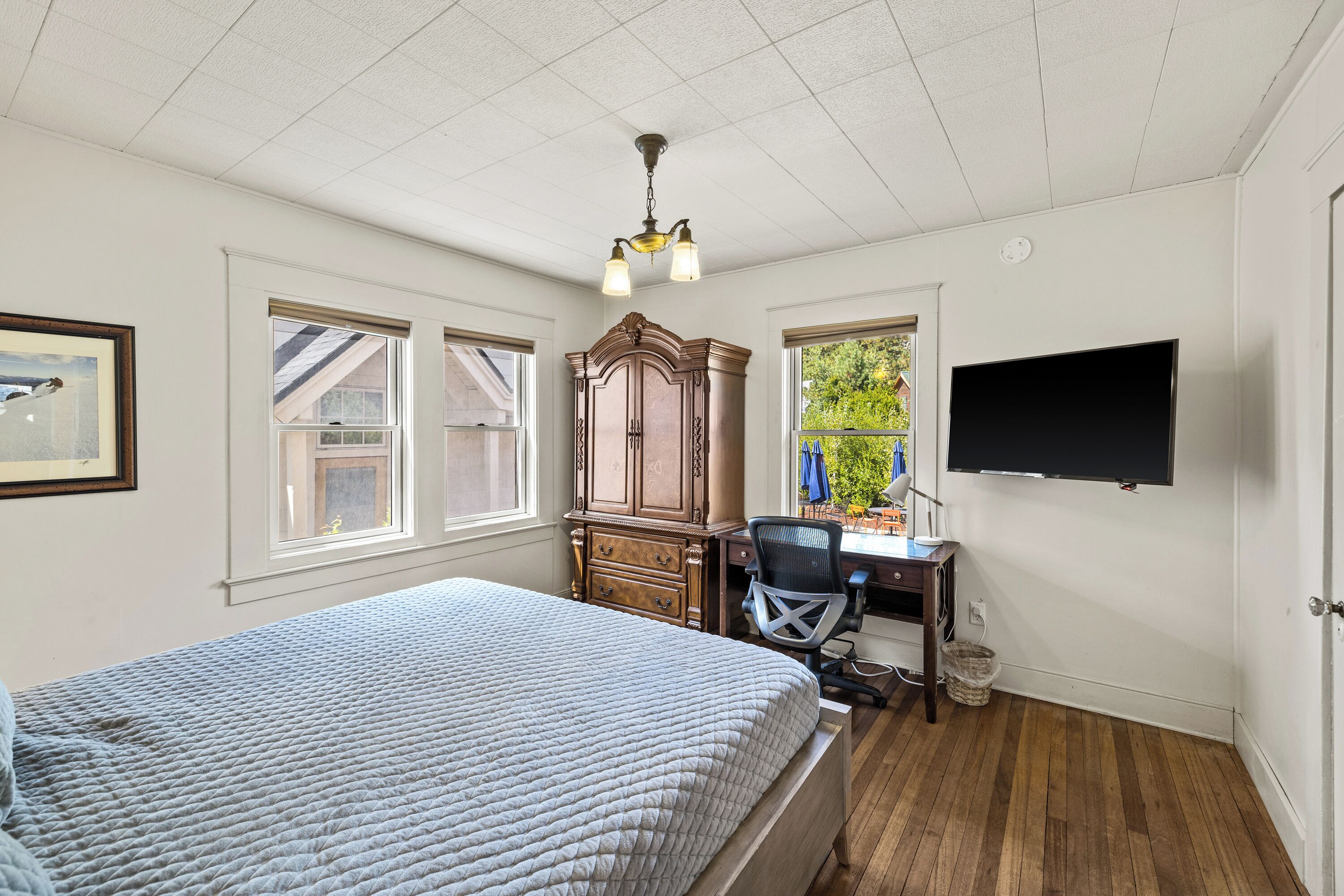 A bedroom with a bed, a desk, a chair, a television, and a window with a view of greenery.