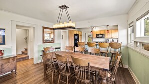 Un comedor con una mesa y sillas de madera, una araña y una cocina al fondo.