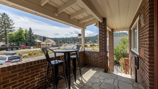 Un patio cubierto con un muro de ladrillo, una mesa con sillas y vista a una zona residencial con árboles y edificios.