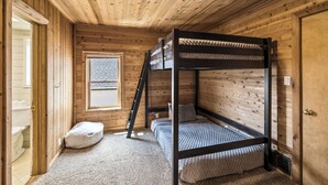 Habitación tipo cabaña de madera con literas, una ventana y una puerta.