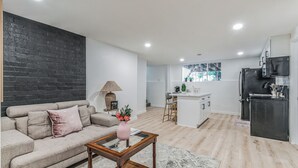 A modern living room with a sofa, a coffee table, and a lamp. There is a kitchen area with a refrigerator and a dining table. - Charming 1-bedroom house in lovely Burien with  high speed WiFi,  (Burien)