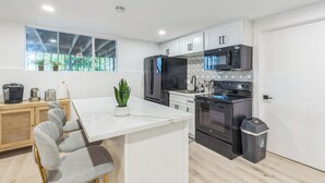 A modern kitchen with white cabinetry, a black refrigerator, a microwave, and an oven. There is a dining area with a white table and grey chairs. - Charming 1-bedroom house in lovely Burien with  high speed WiFi,  (Burien)