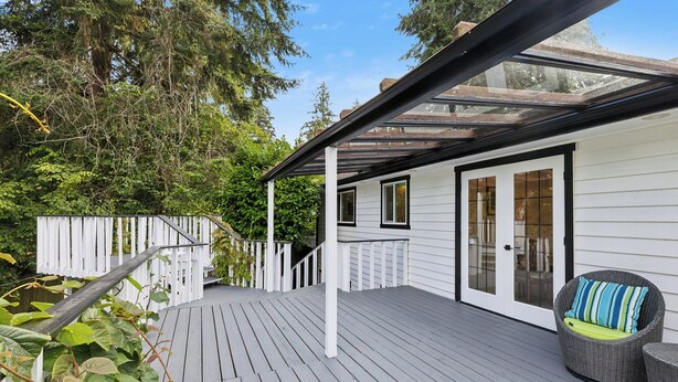 A wooden deck with a glass enclosure, white walls, and a wicker chair with a cushion. - Charming 1-bedroom house in lovely Burien with  high speed WiFi,  (Burien)