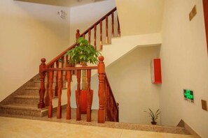 A staircase with wooden balusters, a potted plant, and a red emergency exit sign. - Wuyishan Hike Tea House Inn (Wuyishan)