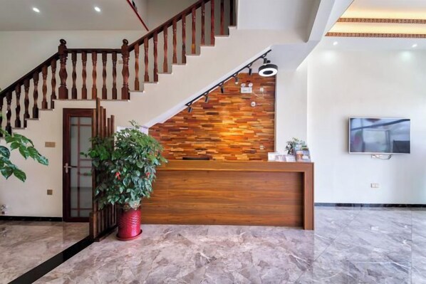 A reception area with a wooden reception desk, a staircase, and a flat-screen TV on the wall. - Wuyishan Hike Tea House Inn (Wuyishan)