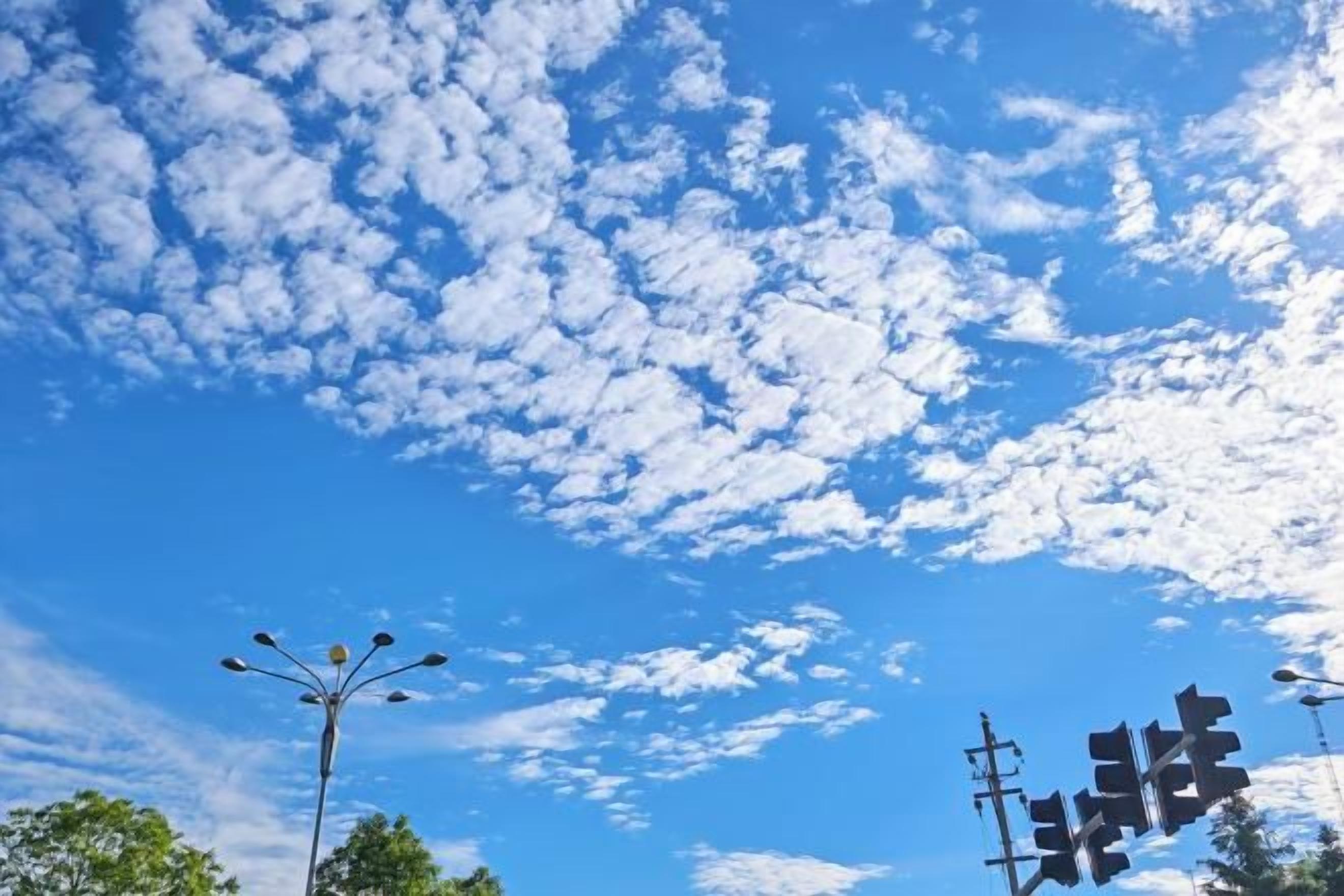 A clear blue sky with scattered clouds and street lamps.