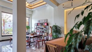 A modern interior with a wooden table and chairs, a bookshelf, and a large plant. - Wuyishan Hike Tea House Inn (Wuyishan)