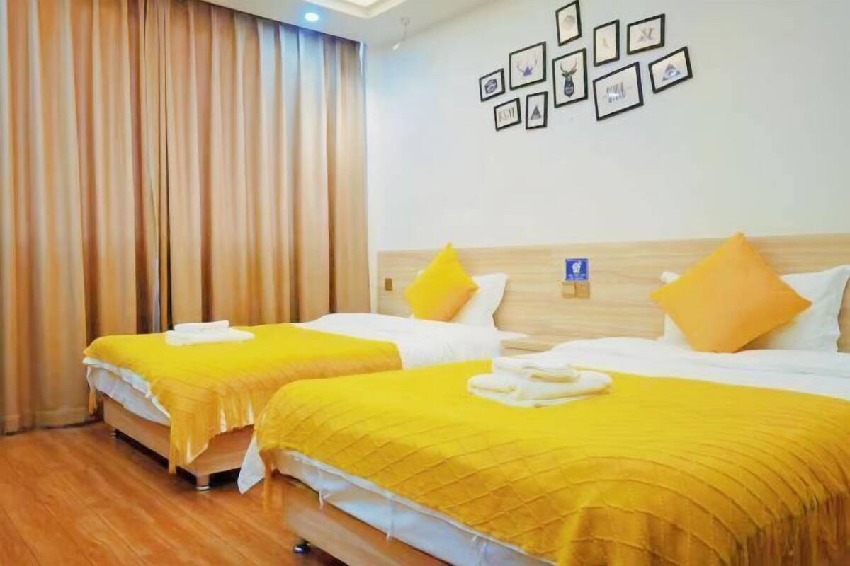 Une chambre d’hôtel avec deux lits, chacun recouvert d’une couvre-lit jaune, agrémenté d’oreillers blancs et doté d’une tête de lit en bois.