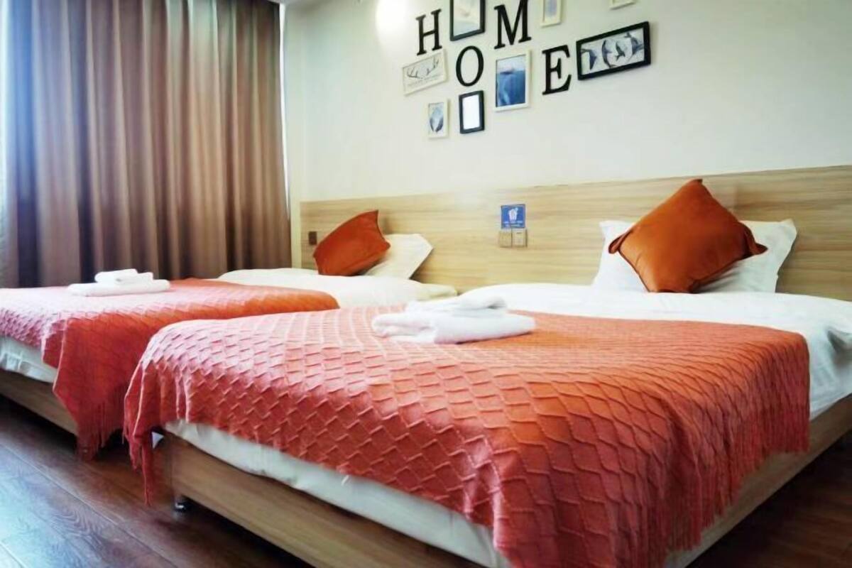 Une chambre d’hôtel avec deux lits, chacun recouvert d’une courtepointe rouge à motifs et agrémenté d’oreillers blancs. Des tableaux encadrés sont accrochés au mur au-dessus des lits.