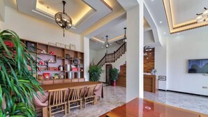 A spacious living area with a wooden dining table, built-in shelves, and a staircase leading to another level. - Wuyishan Hike Tea House Inn (Wuyishan)