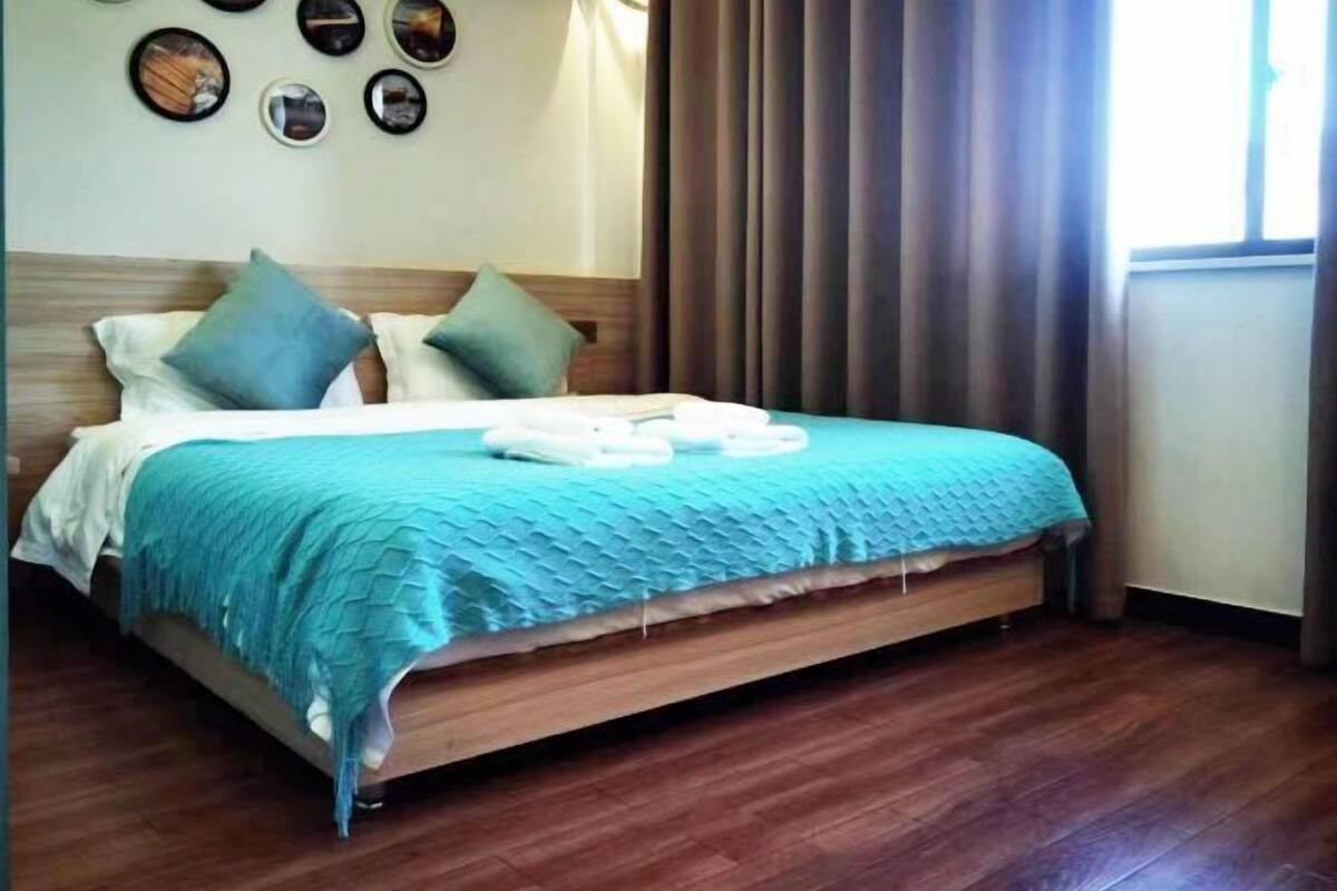 Un lit bien fait, avec une couverture bleue, une tête de lit en bois et un ensemble de serviettes.