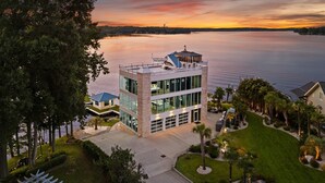 A modern building with a glass facade, a covered outdoor area, and a view of a calm lake at sunset. - The Glass Mansion w/Optional Boat Rental (Terrell)