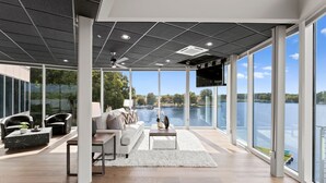 A spacious living area with a large window overlooking a lake, furnished with a sofa, chairs, and a coffee table. - The Glass Mansion w/Optional Boat Rental (Terrell)