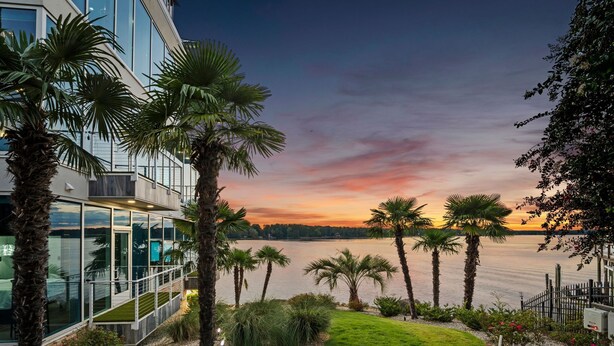 A modern building with large glass windows overlooking a body of water, surrounded by palm trees and a well-maintained lawn. - The Glass Mansion w/Optional Boat Rental (Terrell)