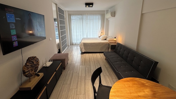 Una habitación de hotel moderna con una cama grande, un sofá, una mesa de comedor y un televisor montado en la pared.