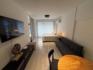 Una habitación de hotel moderna con una cama grande, un sofá, una mesa de comedor y un televisor montado en la pared.