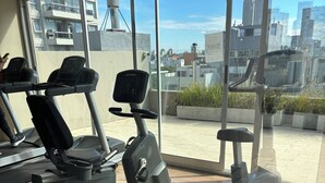 Un gimnasio con cintas de correr, elípticas y máquinas de pesas. Cuenta con ventanas amplias y vistas a la ciudad.