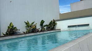 Una piscina con bordes azulejados, rodeada por un muro blanco y plantas.