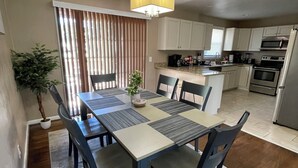 A dining area with a table set for six, surrounded by chairs. A potted plant is on the floor beside the table. - Hidden Gem A Comfortable 4bedroom home with a fenced-in yard. (Portsmouth)
