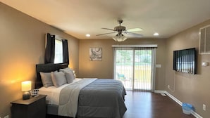 A bedroom with a bed, nightstand, lamp, ceiling fan, and a view of the outdoors through a sliding door. - Hidden Gem A Comfortable 4bedroom home with a fenced-in yard. (Portsmouth)