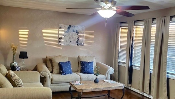 A living room with a ceiling fan, a sofa, a coffee table, and a painting on the wall. - Hidden Gem A Comfortable 4bedroom home with a fenced-in yard. (Portsmouth)
