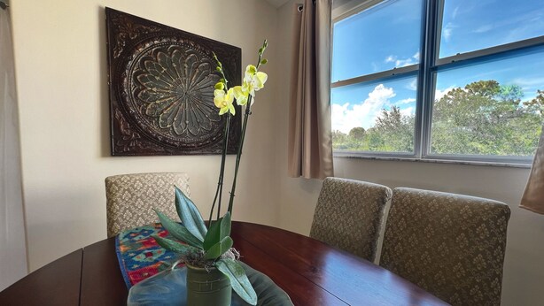 Une table à manger agrémentée d’une orchidée en pot, d’un élément décoratif mural et offrant une vue sur les arbres à travers une fenêtre.
