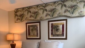Ein Schlafzimmer mit einem Bett, einem Deckenventilator, zwei gerahmten Bildern, einem Nachttisch und einer Lampe.
