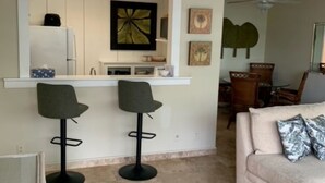 Eine moderne Küche mit zwei Barhocker, ein Essbereich mit einer Couch und Stühlen sowie ein Deckenventilator.