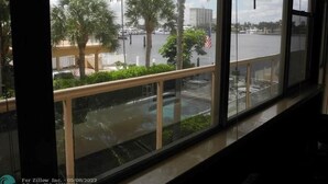 Blick von einem Balkon mit Geländer auf einen Hafen mit Booten und Palmen.
