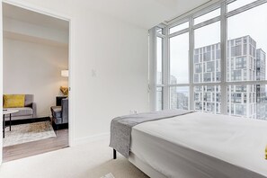 Enjoy a city view from the large window in this stylish room, featuring a comfortable bed, a sofa, and a small table with a lamp.