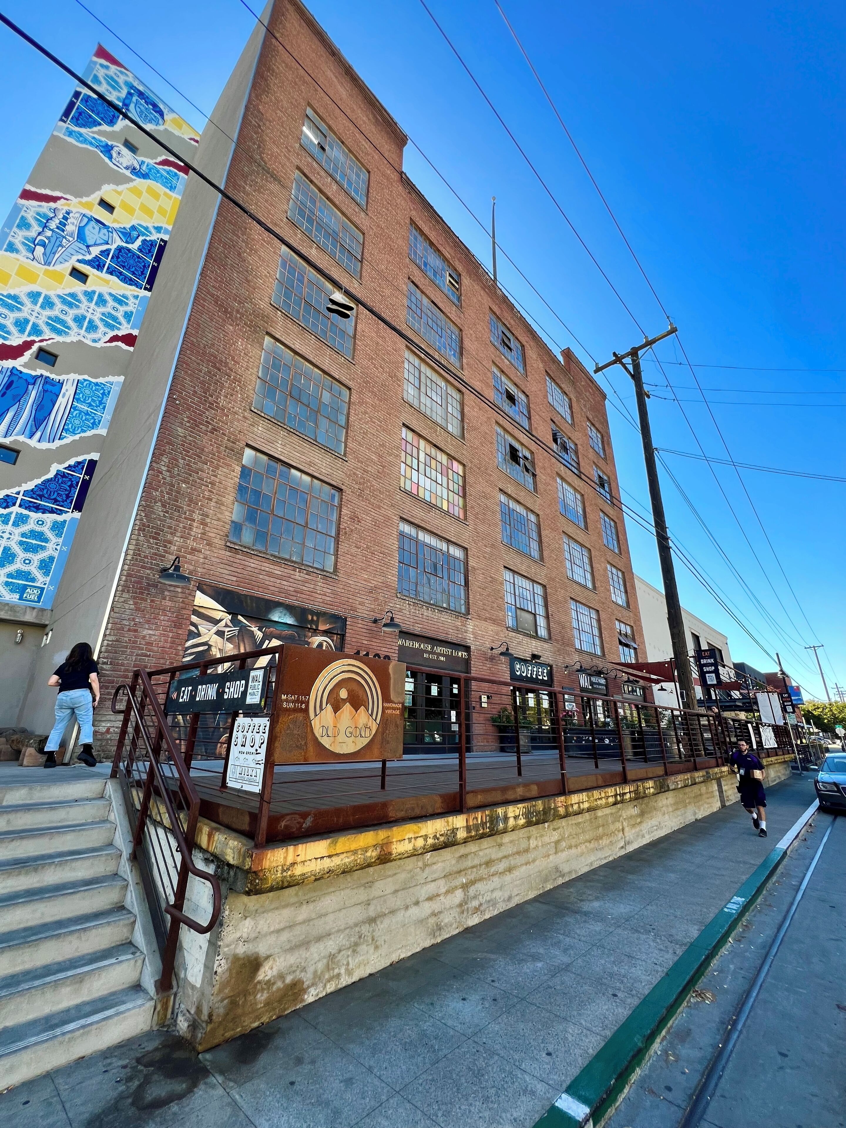 A multi-story building with a brick facade, a mural on the side, and a sign for an eat-drink shop.