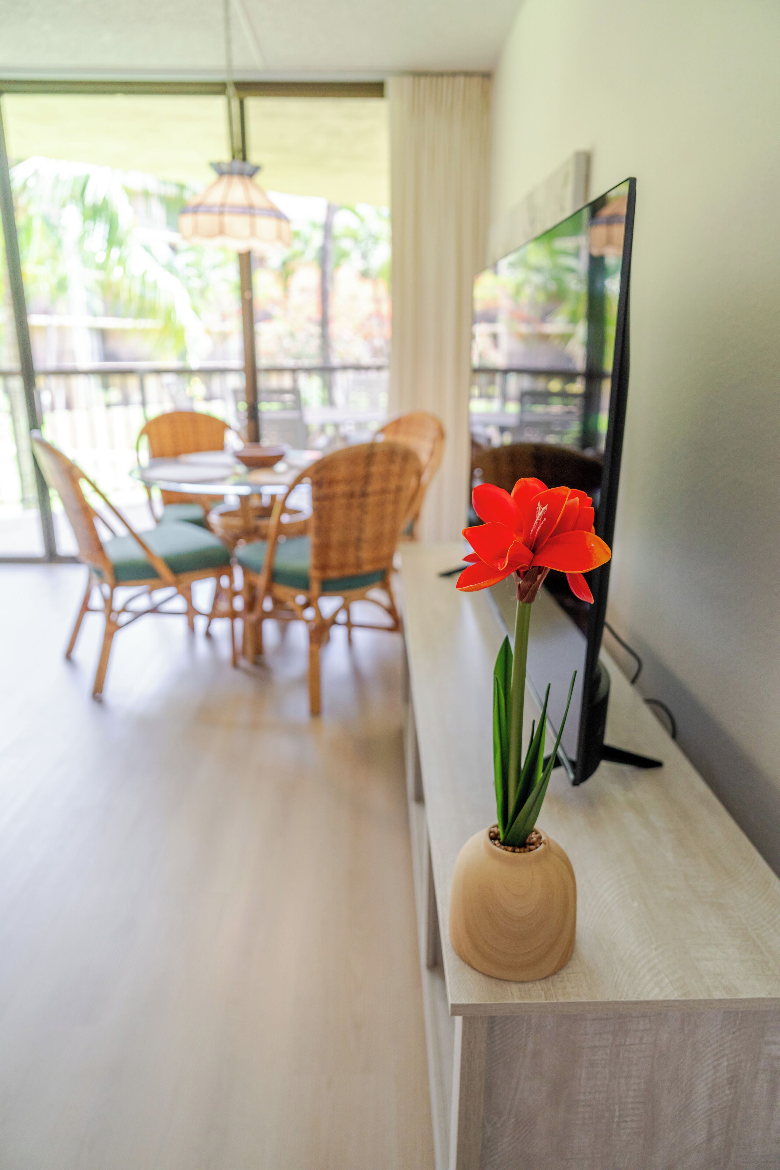 A modern living room with a flat-screen TV, a wooden side table, and a vase with a single red flower.