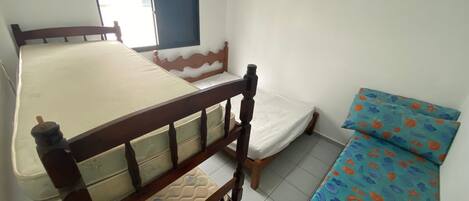 Una habitación con una cama de madera, una cama más pequeña con un colchón colorido y una ventana con persianas.