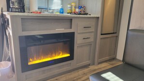 A kitchen with a built-in fireplace, wooden cabinets, and a countertop with various items. - Cozy RV in charming Pikeville with WiFi, AC (Pikeville)