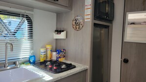 A compact kitchenette with a sink, stove, microwave, and storage cabinets. - Cozy RV in charming Pikeville with WiFi, AC (Pikeville)