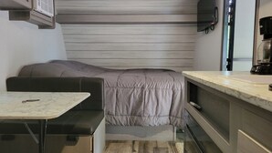 A compact room with a bed, a small table, a kitchenette, and a built-in bench. - Cozy RV in charming Pikeville with WiFi, AC (Pikeville)